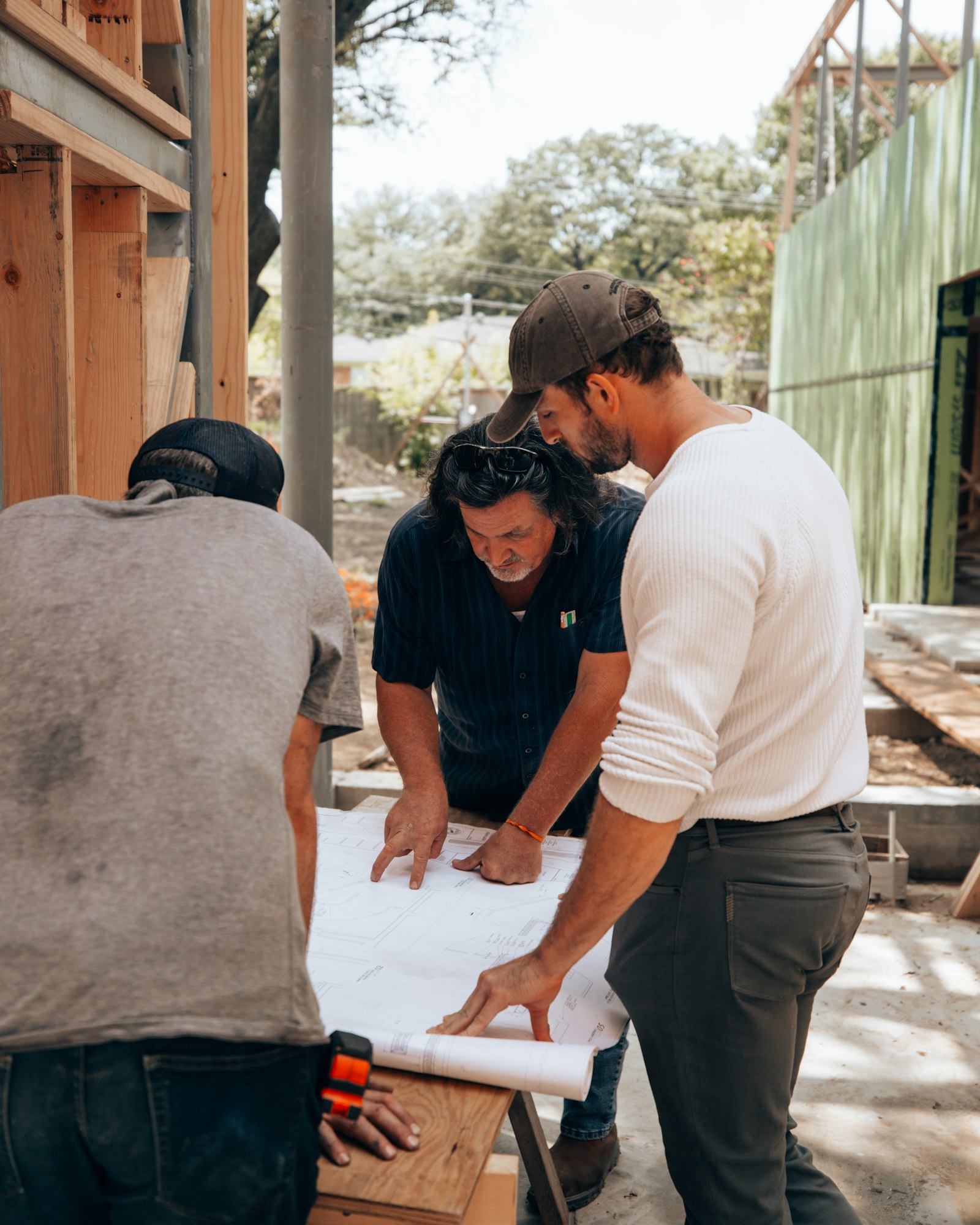 Three men on a building site reading construction drawings spread over a workbench